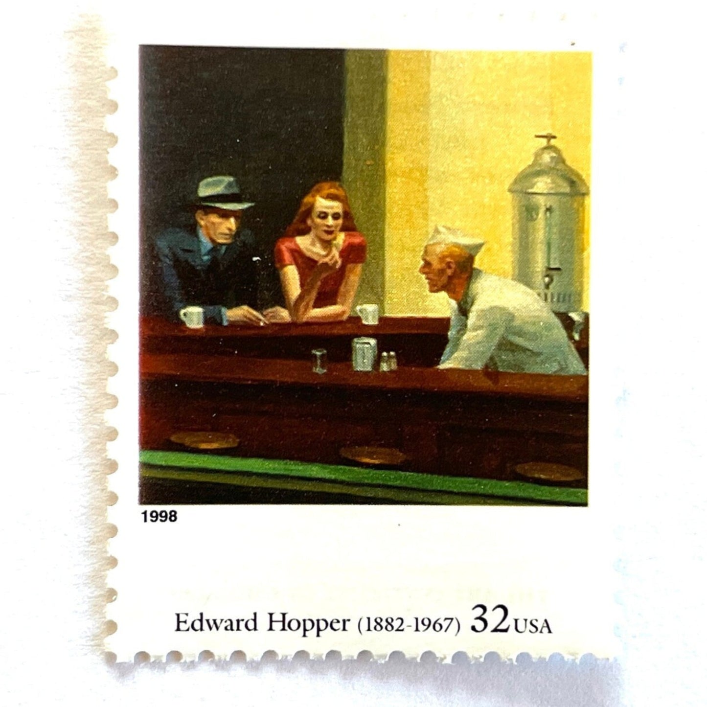 An up close image of Edward Hopper’s “Nighthawks" Postage Stamp from the 1998 Four Centuries of American Art Series. This stamp depicts the iconic painting of a man and woman, both elegantly dressed, sitting at a diner counter late at night drinking coffee, while a waiter, dressed in white, prepares their pie. An iconic urban living theme, this stamp depicts the classic American diner experience. These are vintage unused USPS postage stamps with a face value of 32 cents each. Scott number 3236P.