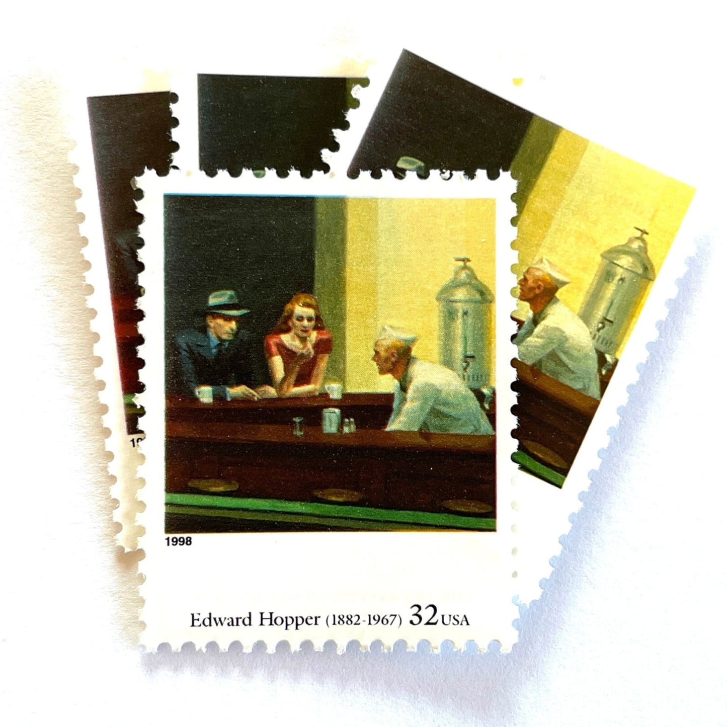 Edward Hopper’s “Nighthawks" Postage Stamp from the 1998 Four Centuries of American Art Series. This stamp depicts the iconic painting of a man and woman, both elegantly dressed, sitting at a diner counter late at night drinking coffee, while a waiter, dressed in white, prepares their pie. An iconic urban living theme, this stamp depicts the classic American diner experience. These are vintage unused USPS postage stamps with a face value of 32 cents each. Scott number 3236P.