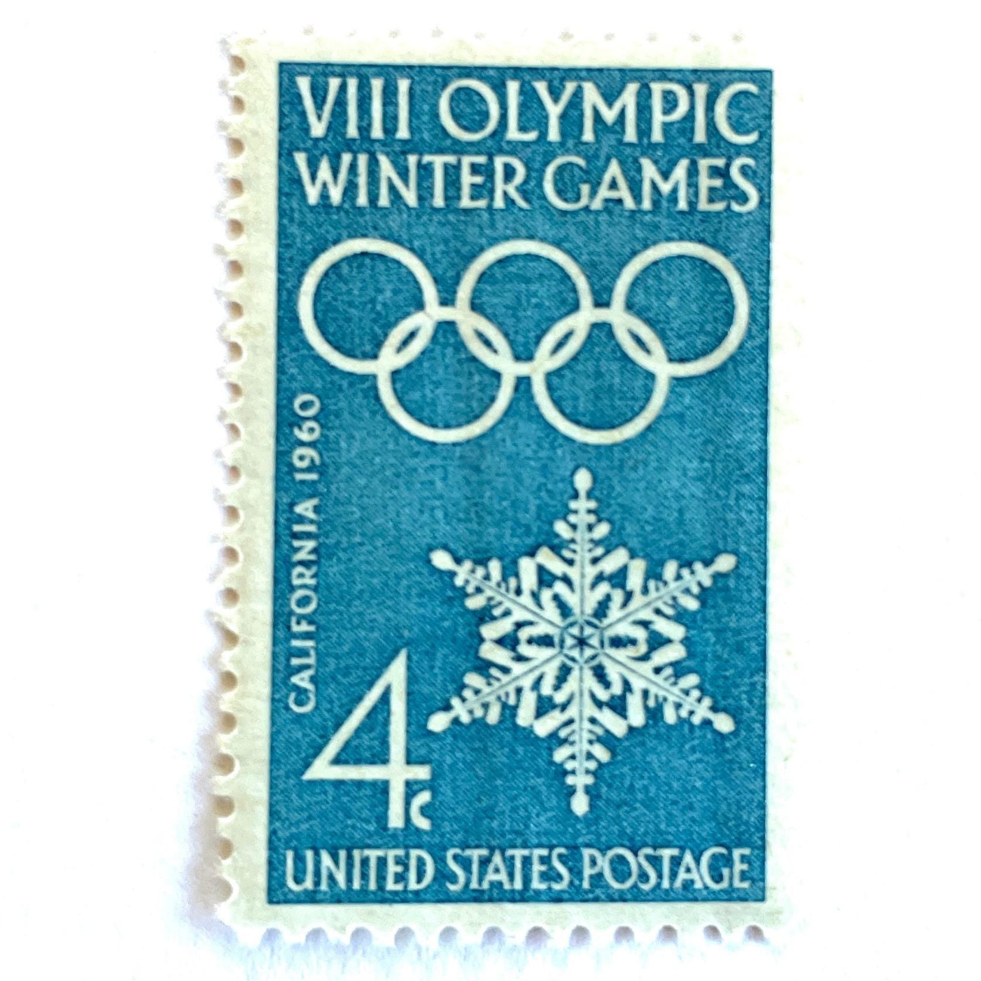 Image of 1960 “VIII Olympic Winter Games” 4-cent mail stamps. Scott #1146. Stamp Themes: 1960 Winter Olympics, Olympic Games, Olympic Rings, Olympiad, Olympic Valley, Lake Tahoe, Squaw Valley, Palisades at Tahoe, Sierra Nevada, California, Snowflake, Winter Postage Stamp. Blue postage stamp.