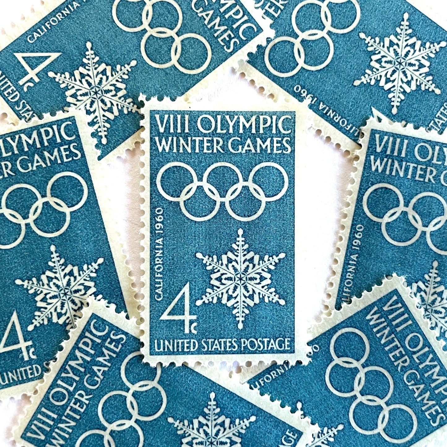 Image of 1960 “VIII Olympic Winter Games” 4-cent mail stamps. Scott #1146. Stamp Themes: 1960 Winter Olympics, Olympic Games, Olympic Rings, Olympiad, Olympic Valley, Lake Tahoe, Squaw Valley, Palisades at Tahoe, Sierra Nevada, California, Snowflake, Winter Postage Stamp. Blue postage stamp.