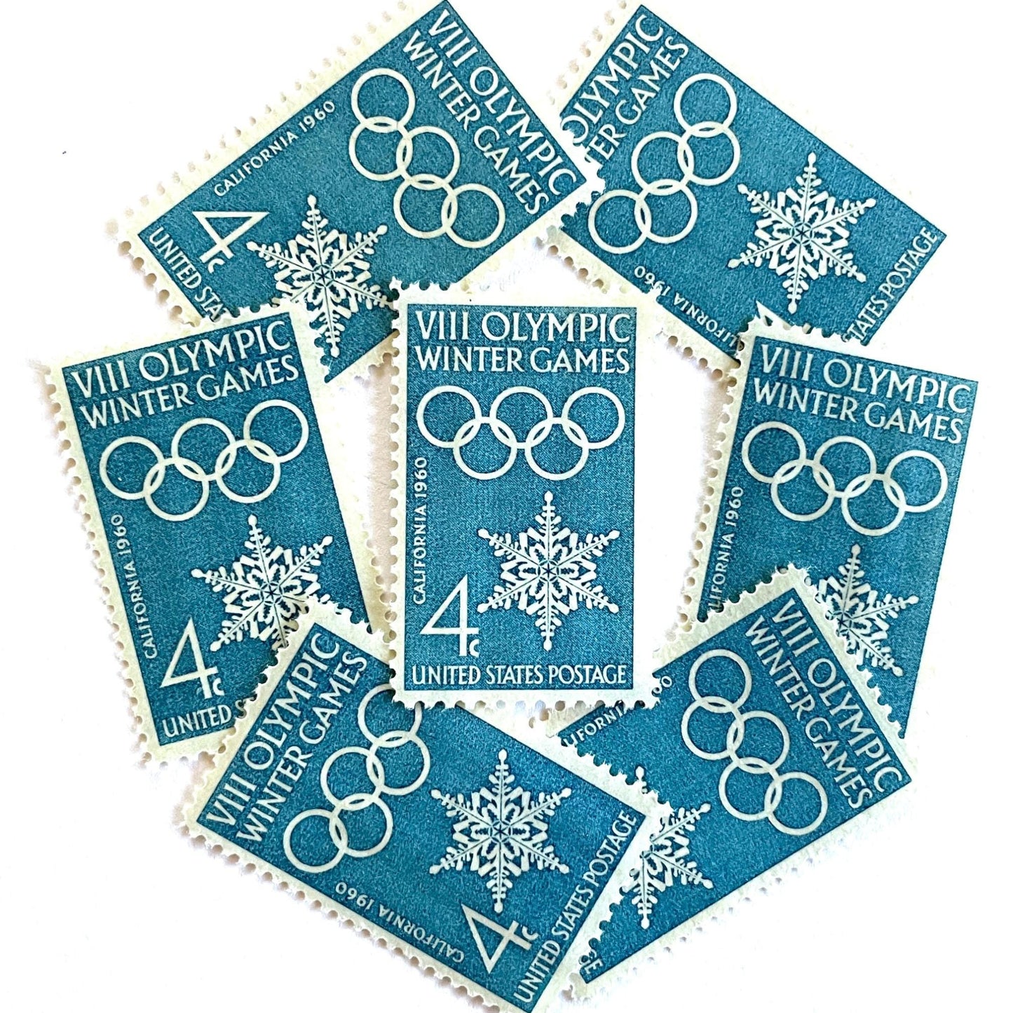 Image of 1960 “VIII Olympic Winter Games” 4-cent mail stamps. Scott #1146. Stamp Themes: 1960 Winter Olympics, Olympic Games, Olympic Rings, Olympiad, Olympic Valley, Lake Tahoe, Squaw Valley, Palisades at Tahoe, Sierra Nevada, California, Snowflake, Winter Postage Stamp. Blue postage stamp.