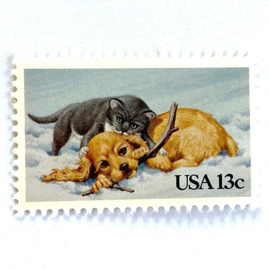 Image of 1982 Christmas Issue “Kitten and Puppy” 13-cent stamps. Scott #2025. Stamp Themes: Pets, Cat, Dog, Humane Society, Play, Snow, Winter. Light Blue postage stamp.