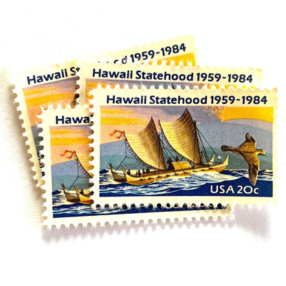 Image of Hawaii Statehood postage stamps from 1984, featuring a Polynesian voyaging canoe on the ocean, a golden plover in flight, and an erupting Mauna Loa volcano on vintage unused 20-cent USPS postage, Scott 2080.