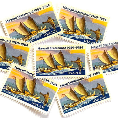 Image of Hawaii Statehood postage stamps from 1984, featuring a Polynesian voyaging canoe on the ocean, a golden plover in flight, and an erupting Mauna Loa volcano on vintage unused 20-cent USPS postage, Scott 2080.