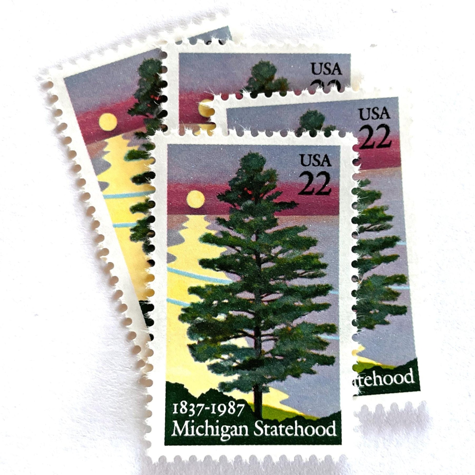 Image of Michigan Statehood postage stamps from 1987, featuring a white pine tree before a sunrise over Lake Huron on vintage unused 22-cent USPS postage, Scott 2246.
