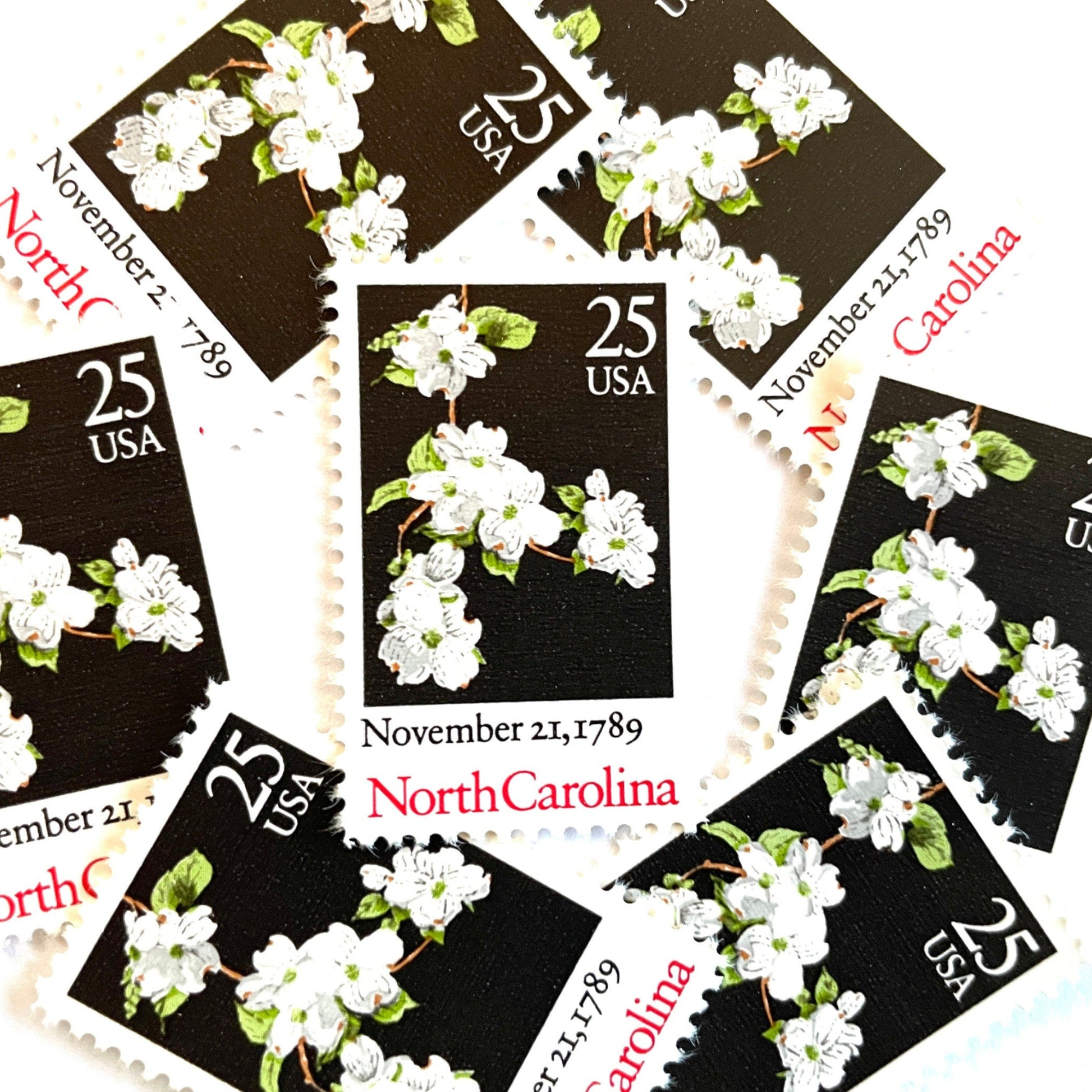 Image of North Carolina Statehood postage stamps from the 1989 Bicentenary Statehood series, featuring white dogwood flowers on a black background on vintage unused 25-cent USPS postage, Scott 2347.