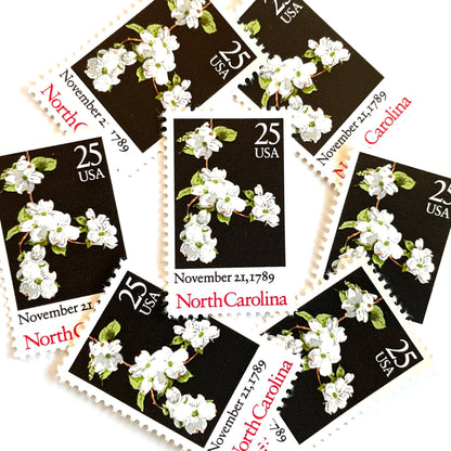 Image of North Carolina Statehood postage stamps from the 1989 Bicentenary Statehood series, featuring white dogwood flowers on a black background on vintage unused 25-cent USPS postage, Scott 2347.