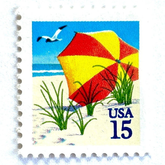Vintage 1990 Beach Umbrella postage stamp from the USPS Mini-Scapes series featuring a red and yellow umbrella on a sandy beach with a seagull and blue sky on unused 15-cent USPS postage, Scott 2443.