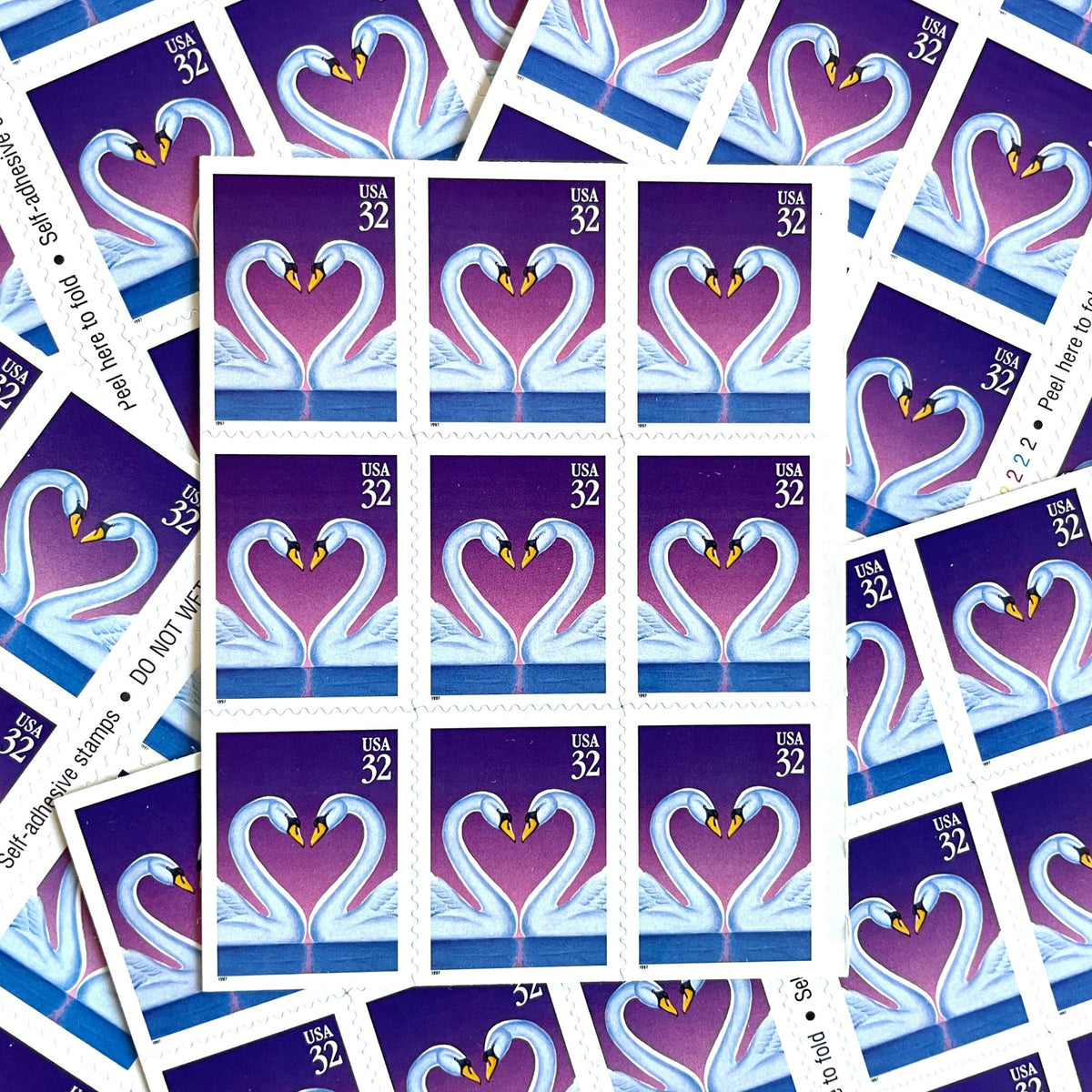 Love Swans postage stamps from 1997 featuring two white swans facing one another with their curved necks forming a heart against a purple background on vintage unused 32-cent USPS postage, Scott 3123.