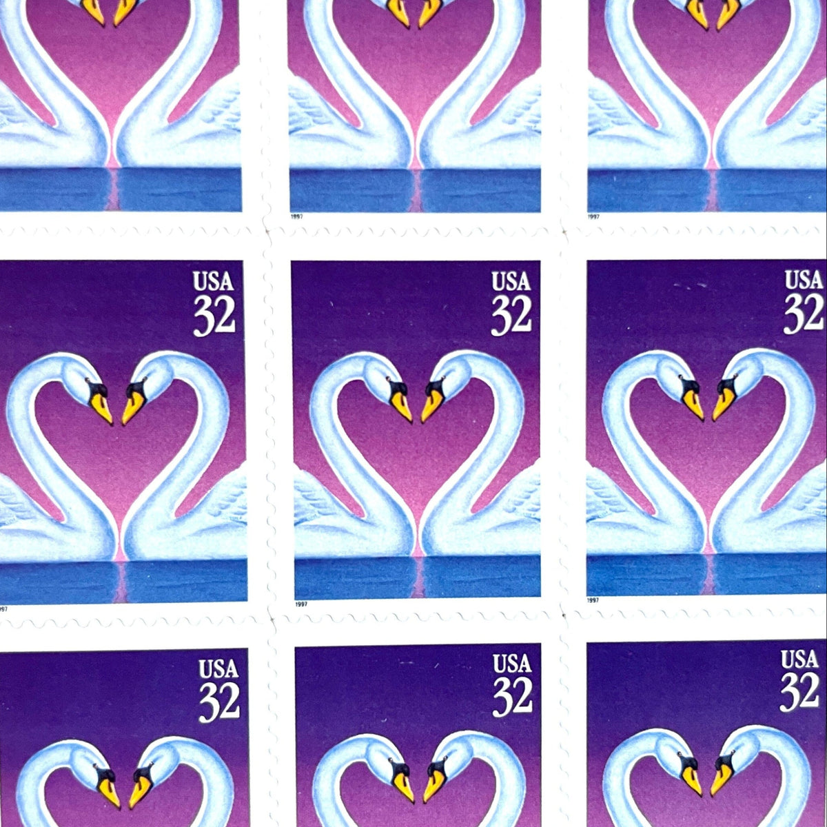 Love Swans postage stamps from 1997 featuring two white swans facing one another with their curved necks forming a heart against a purple background on vintage unused 32-cent USPS postage, Scott 3123.