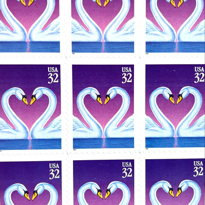 Love Swans postage stamps from 1997 featuring two white swans facing one another with their curved necks forming a heart against a purple background on vintage unused 32-cent USPS postage, Scott 3123.