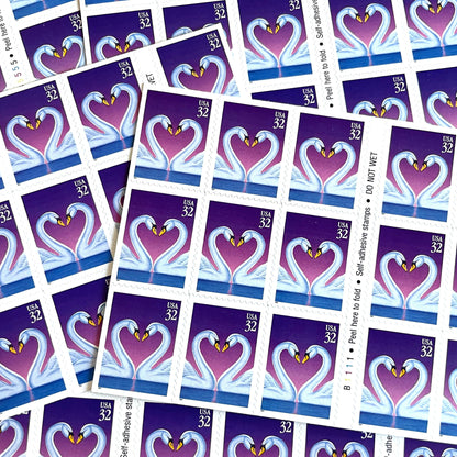 Love Swans postage stamps from 1997 featuring two white swans facing one another with their curved necks forming a heart against a purple background on vintage unused 32-cent USPS postage, Scott 3123.