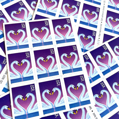 Love Swans postage stamps from 1997 featuring two white swans facing one another with their curved necks forming a heart against a purple background on vintage unused 32-cent USPS postage, Scott 3123.