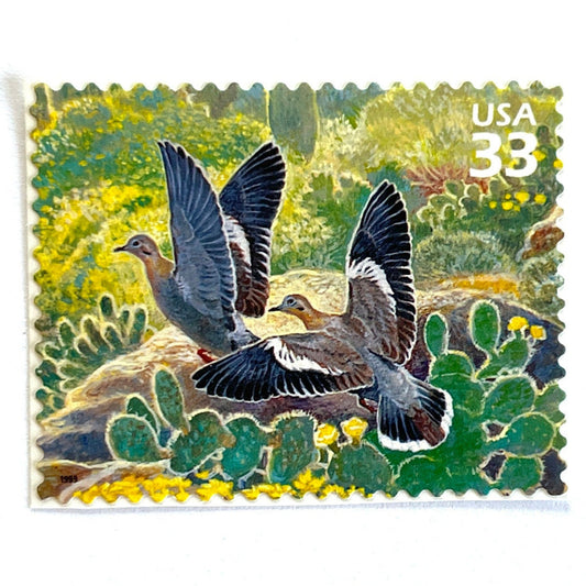Image of White-winged Dove postage stamps from the 1999 Nature of America Sonoran Desert issue, featuring a gray desert dove in a Southwestern landscape of green cactus and yellow flowers on vintage unused 33-cent USPS postage, Scott 3293c.
