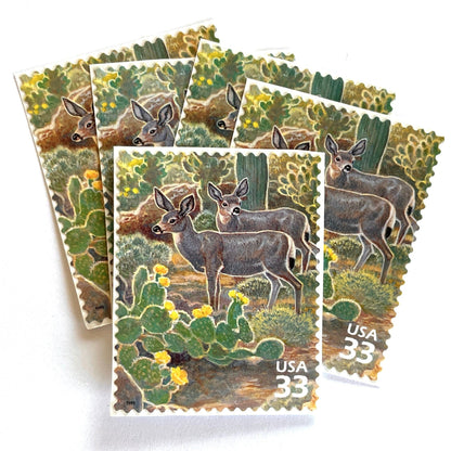 Image of Desert Mule Deer postage stamps from the 1999 Nature of America Sonoran Desert series, featuring brown mule deer standing amongst green cactus with yellow flowers in a Southwestern desert landscape on vintage unused 33-cent USPS postage, Scott 3293f.