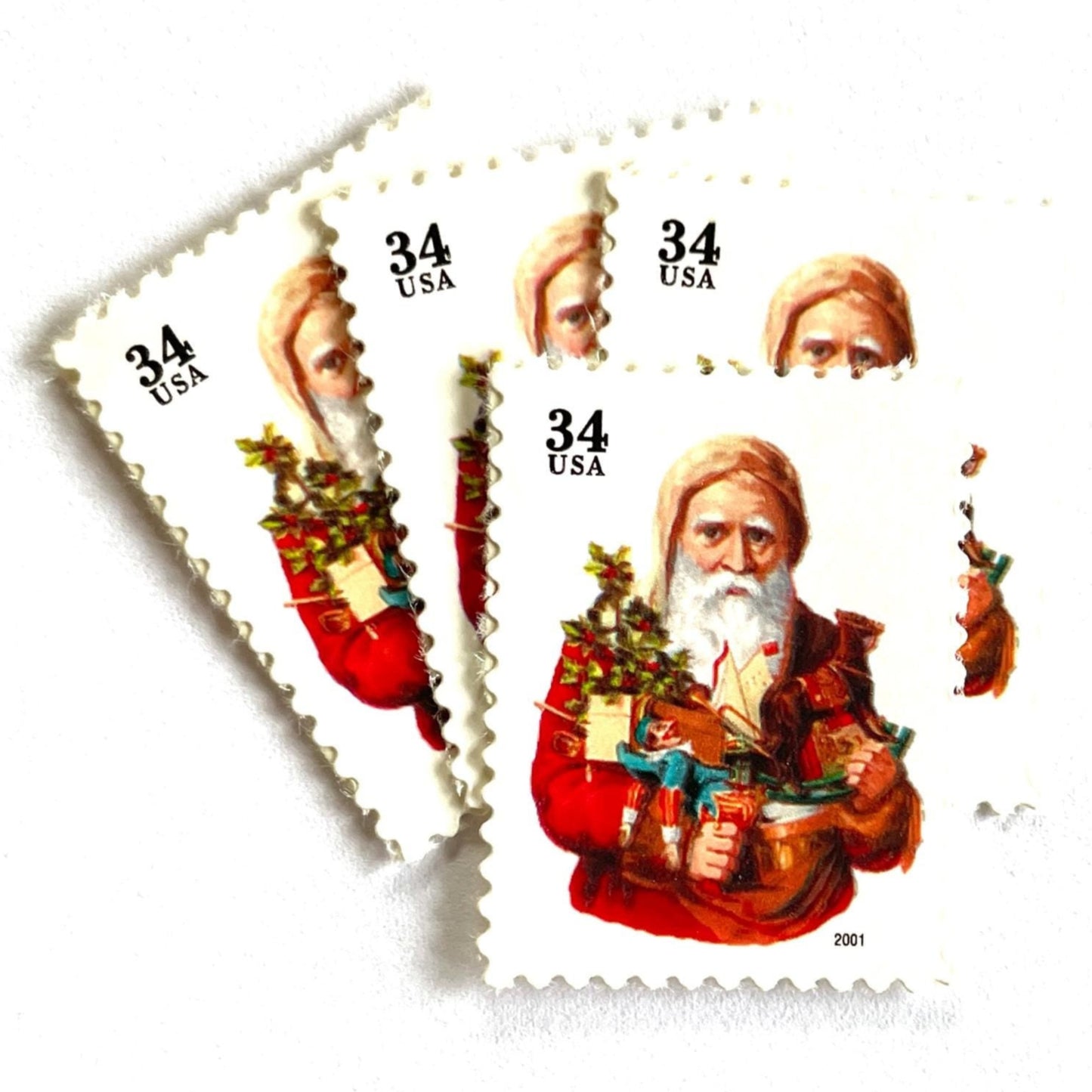 Image of 34-cent Contemporary Christmas Santa Claus Se-tenant “Santa with Toy Horse” USPS postage stamp featuring a relatively skinny white bearded Santa wearing a brown, hooded robe over a red suit. This sober looking Santa is holding a bounty of toys and gifts for children, including a doll dressed in blue and white, a small evergreen tree decorated with garland, and a rocking horse. Scott #3537. Stamp themes: Christmas, holidays, winter, Santa Claus, toys, gifts, winter wedding, winter save-the-date. Red