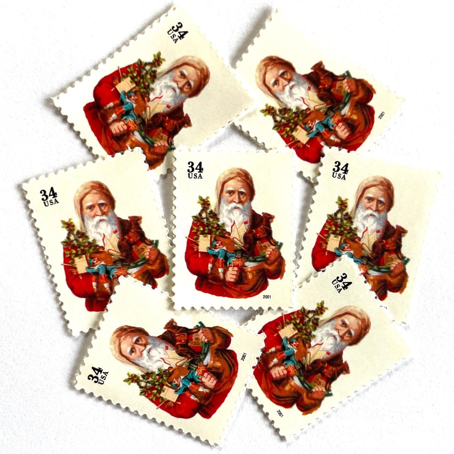 Image of 34-cent Contemporary Christmas Santa Claus Se-tenant “Santa with Toy Horse” USPS postage stamp featuring a relatively skinny white bearded Santa wearing a brown, hooded robe over a red suit. This sober looking Santa is holding a bounty of toys and gifts for children, including a doll dressed in blue and white, a small evergreen tree decorated with garland, and a rocking horse. Scott #3537. Stamp themes: Christmas, holidays, winter, Santa Claus, toys, gifts, winter wedding, winter save-the-date. Red