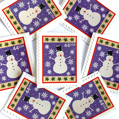 Image of 44-cent Contemporary Christmas Winter Holidays Snowman USPS postage stamp featuring a white snowman and snowflakes against a purple background with a design reminiscent of Christmas wrapping paper. Scott #4426. Stamp themes: Christmas, holidays, winter, snow, snowflakes, winter wedding, winter save-the-date. Purple postage stamp.