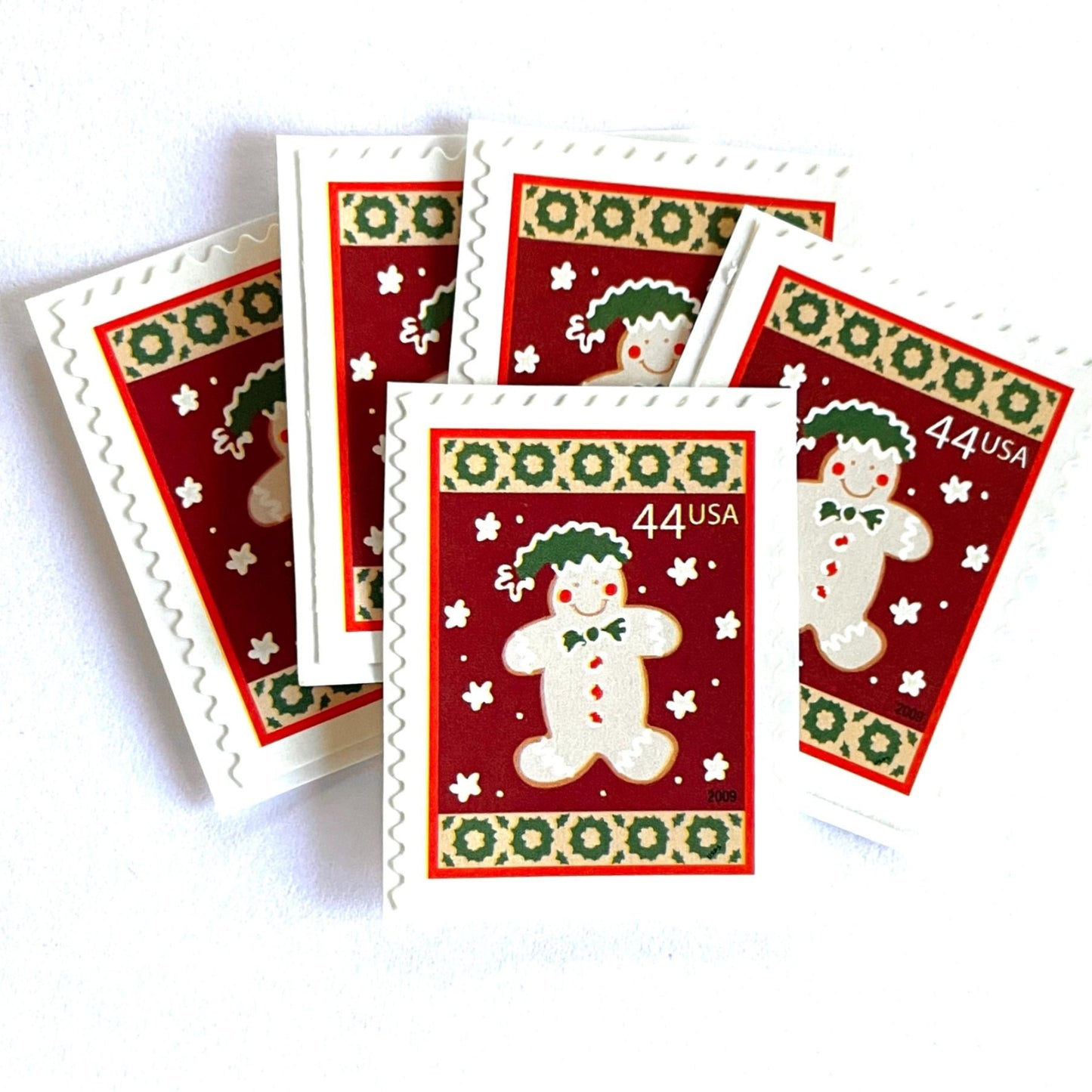 Image of 44-cent Contemporary Christmas Winter Holidays Gingerbread Man USPS postage stamp featuring a beige gingerbread man and snowflakes against a red background with a design reminiscent of Christmas wrapping paper. Scott #4427. Stamp themes: Christmas, holidays, winter, snowflakes, baking, icing, cookies, winter wedding, winter save-the-date. Red postage stamp.