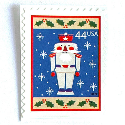 Image of 44-cent Contemporary Christmas Winter Holidays Toy Soldier USPS postage stamp featuring a smiling toy soldier standing at attention, set against a blue background with white snowflakes falling, evoking the imagery of classic holiday stories like “The Nutcracker,” with a design reminiscent of Christmas wrapping paper. Scott #4428. Stamp themes: Christmas, holidays, winter, snowflakes, toys, wooden toys, nutcracker, German, winter wedding, winter save-the-date. Blue postage stamp.