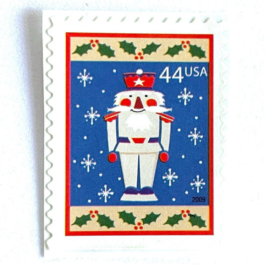 Image of 44-cent Contemporary Christmas Winter Holidays Toy Soldier USPS postage stamp featuring a smiling toy soldier standing at attention, set against a blue background with white snowflakes falling, evoking the imagery of classic holiday stories like “The Nutcracker,” with a design reminiscent of Christmas wrapping paper. Scott #4428. Stamp themes: Christmas, holidays, winter, snowflakes, toys, wooden toys, nutcracker, German, winter wedding, winter save-the-date. Blue postage stamp.
