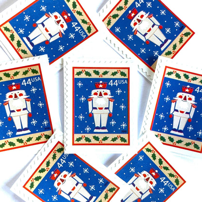 Image of 44-cent Contemporary Christmas Winter Holidays Toy Soldier USPS postage stamp featuring a smiling toy soldier standing at attention, set against a blue background with white snowflakes falling, evoking the imagery of classic holiday stories like “The Nutcracker,” with a design reminiscent of Christmas wrapping paper. Scott #4428. Stamp themes: Christmas, holidays, winter, snowflakes, toys, wooden toys, nutcracker, German, winter wedding, winter save-the-date. Blue postage stamp.