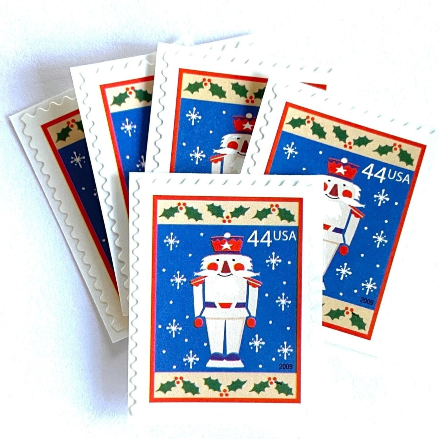 Image of 44-cent Contemporary Christmas Winter Holidays Toy Soldier USPS postage stamps featuring a smiling toy soldier standing at attention, set against a blue background with white snowflakes falling, evoking the imagery of classic holiday stories like “The Nutcracker,” with a design reminiscent of Christmas wrapping paper. Scott #4428. Stamp themes: Christmas, holidays, winter, snowflakes, toys, wooden toys, nutcracker, German, winter wedding, winter save-the-date. Blue postage stamp.