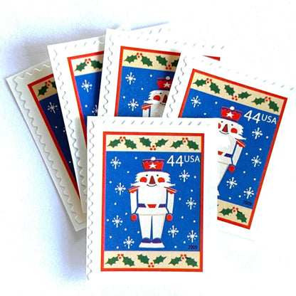 Image of 44-cent Contemporary Christmas Winter Holidays Toy Soldier USPS postage stamps featuring a smiling toy soldier standing at attention, set against a blue background with white snowflakes falling, evoking the imagery of classic holiday stories like “The Nutcracker,” with a design reminiscent of Christmas wrapping paper. Scott #4428. Stamp themes: Christmas, holidays, winter, snowflakes, toys, wooden toys, nutcracker, German, winter wedding, winter save-the-date. Blue postage stamp.