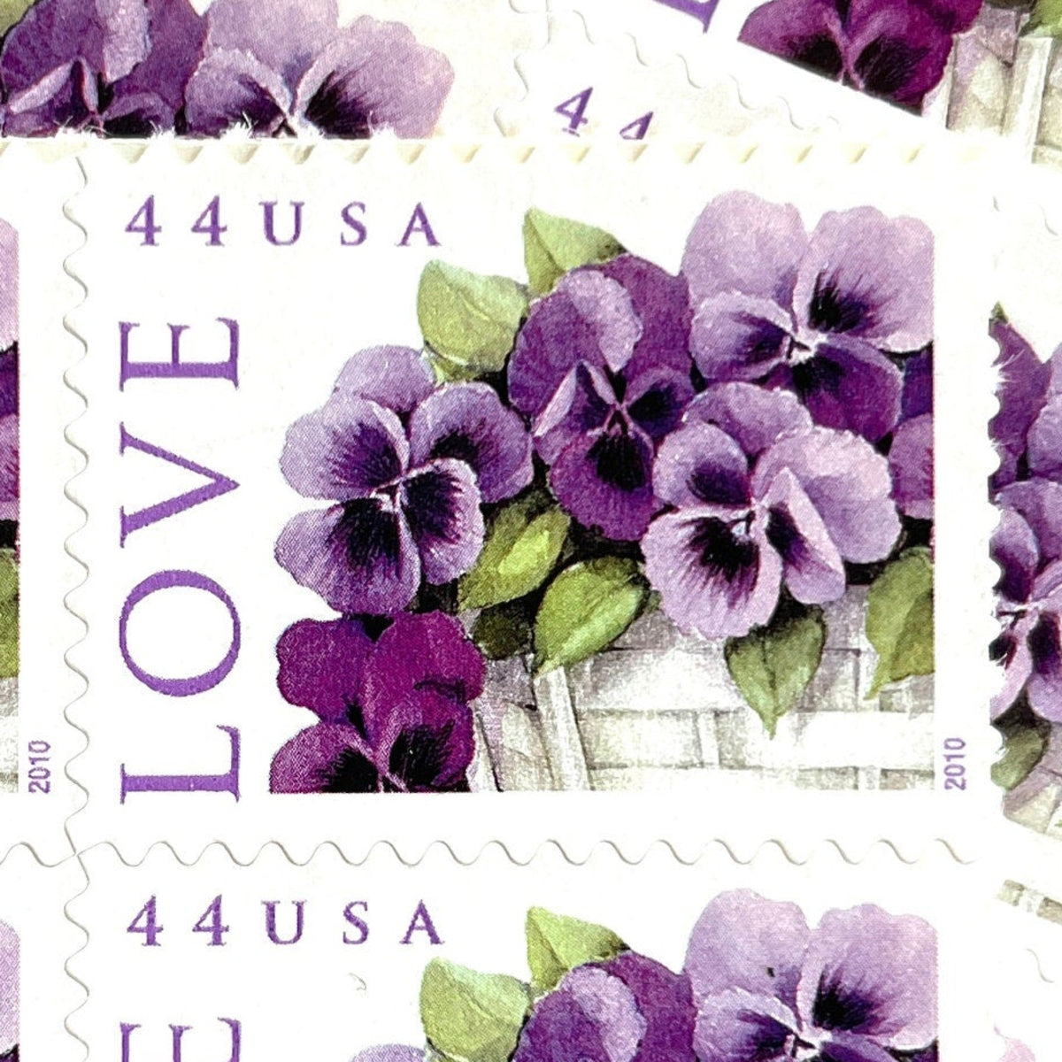 Pansies in a Basket postage stamp from 2010 featuring purple pansies and green foliage in a white woven cart on vintage unused 44-cent USPS postage, Scott 4450.