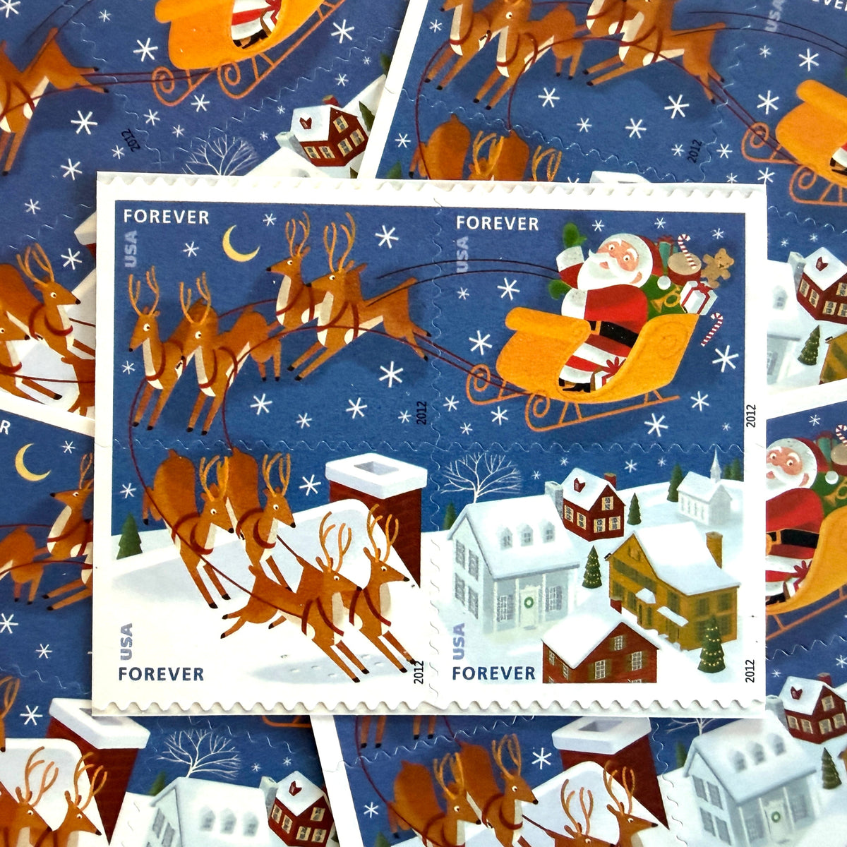 Santa and Sleigh four-stamp se-tenant postage sets from 2012 featuring Santa, flying reindeer, moonlit sky, and snow-covered rooftops on unused USPS Forever postage, Scott 4715a.