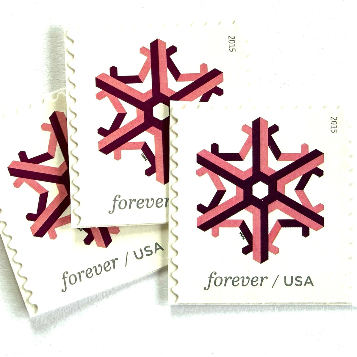 Pink and dark red Geometric Snowflake postage stamps from 2015 featuring a stylized crystalline winter design on unused USPS Forever postage, Scott 5034.