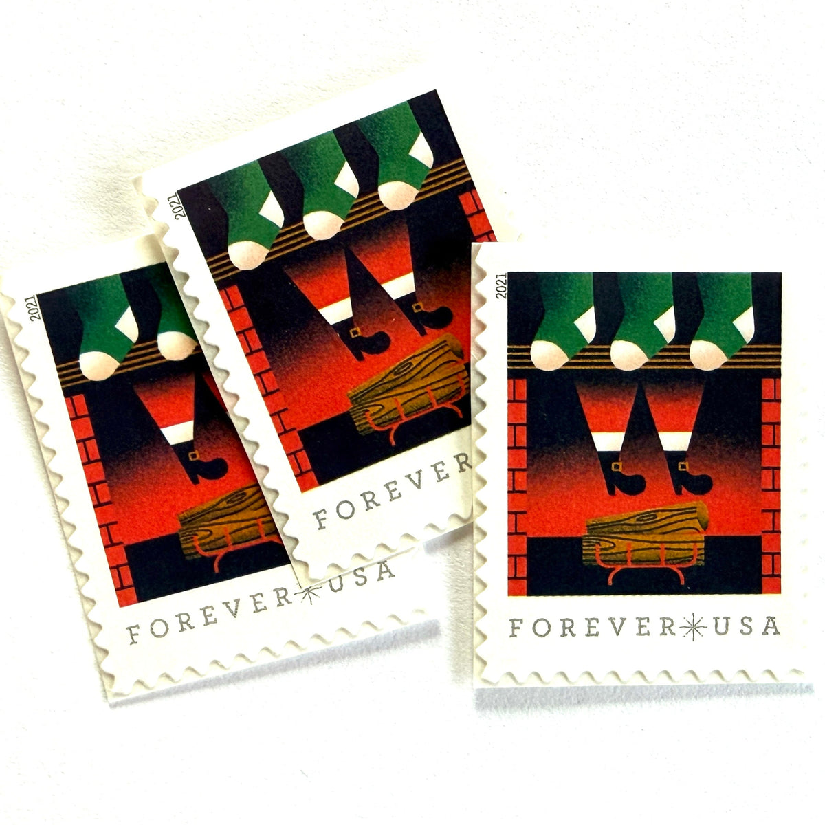 Santa Descending Chimney postage stamps from 2021 featuring St. Nick’s black-booted legs above a red-brick fireplace with green stockings on unused USPS Forever postage, Scott 5645.