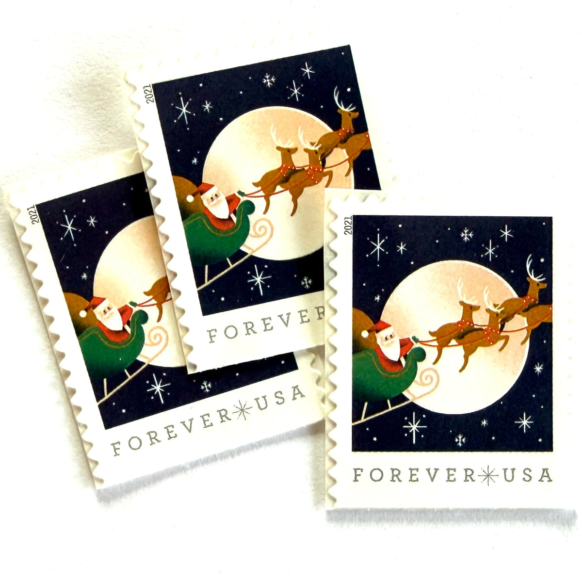 Santa Claus, Sleigh, and Reindeer in Flight postage stamps from 2021 featuring St. Nick and four reindeer flying across a full moon in a dark star-filled sky on unused USPS Forever postage, Scott 5647.