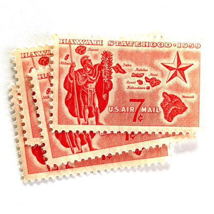 Image of Hawaii Statehood airmail postage stamps from 1959, featuring a Hawaiian Aliʻi extending a lei, a map of the Hawaiian Islands, and a star of statehood on vintage unused 7-cent USPS postage, Scott C55.